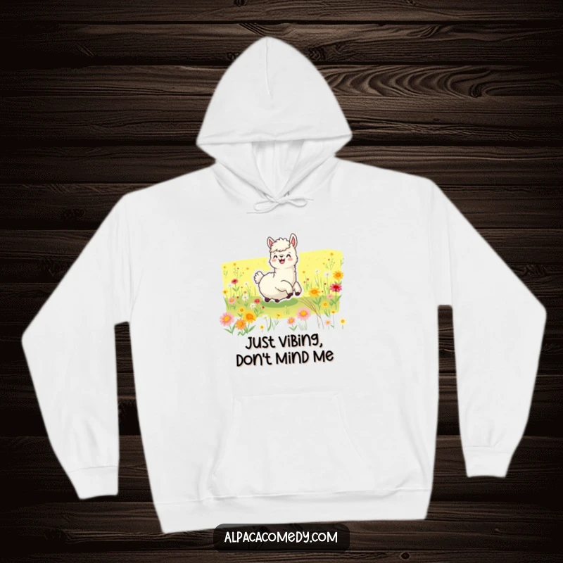 Funny hoodie showcasing a joyful alpaca blissfully rolling amidst a vibrant meadow carpeted with diverse wildflowers, radiating happiness.