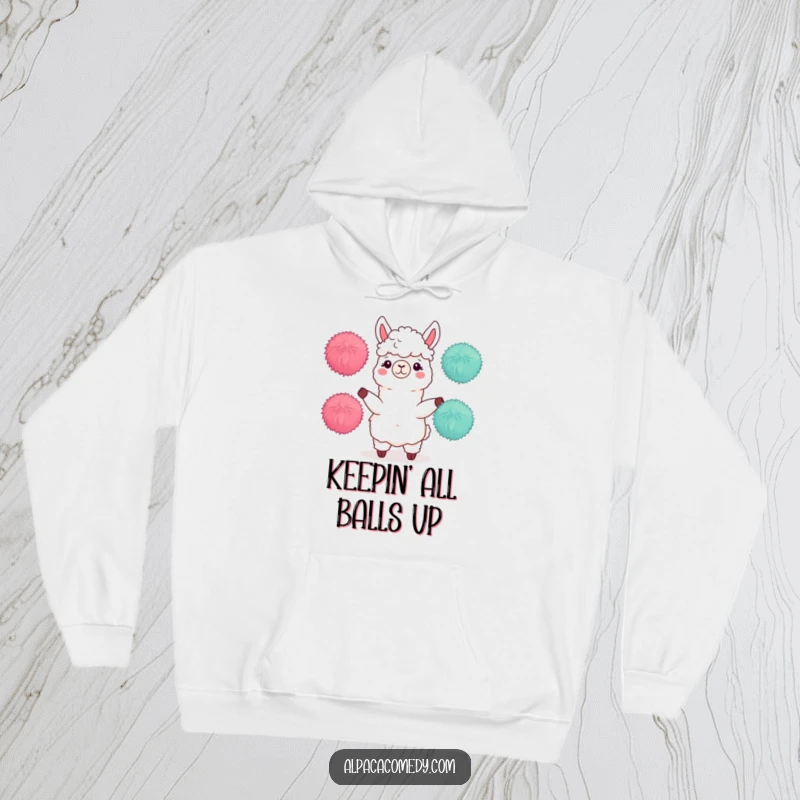 Funny hoodie depicting an alpaca character actively juggling three soft, round pom-poms with impressive dexterity and a focused expression.