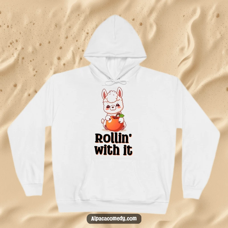 Funny hoodie depicting an alpaca character playfully nudging a rolling apple, suggesting curiosity and a gentle, exploratory spirit.