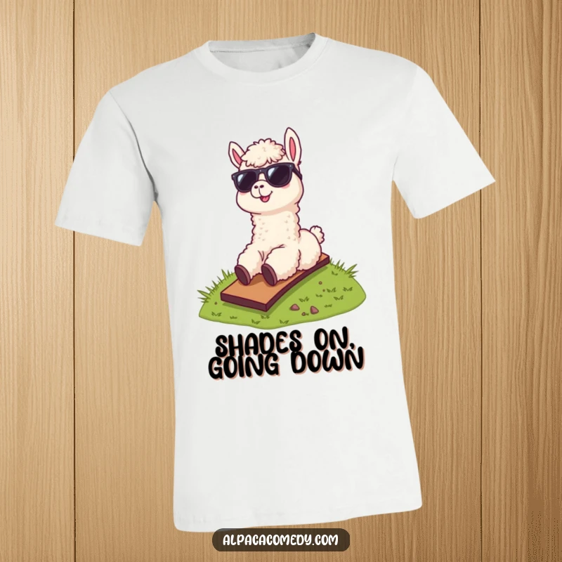 Funny t-shirt depicting a cool alpaca wearing sunglasses, confidently sliding down a grassy hill, embodying fun and adventure.